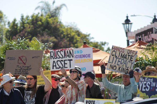 A crowd of people is holding up signs as they protest along Carlsbad Boulevard.