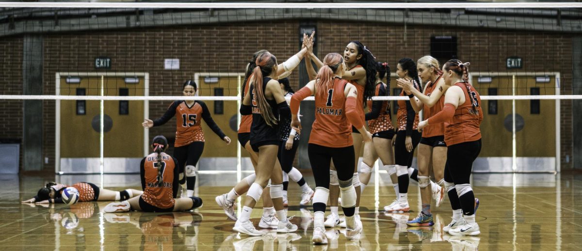 Palomar volleyball players in red celebrate with a high five and applause in the middle of the court.
