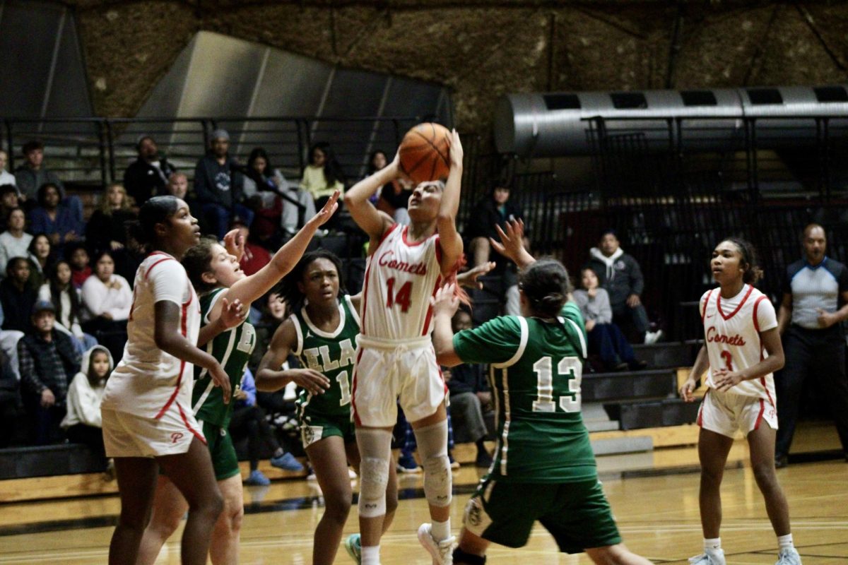 Guard, Kylee Trujillo (#14) is wearing a white and red uniform, jumping with the basketball, trying to make a shot while three of the ELAC players attempt to block her.