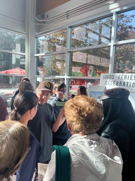 A group of people gather around a table with a sign on top that displays words in French.
