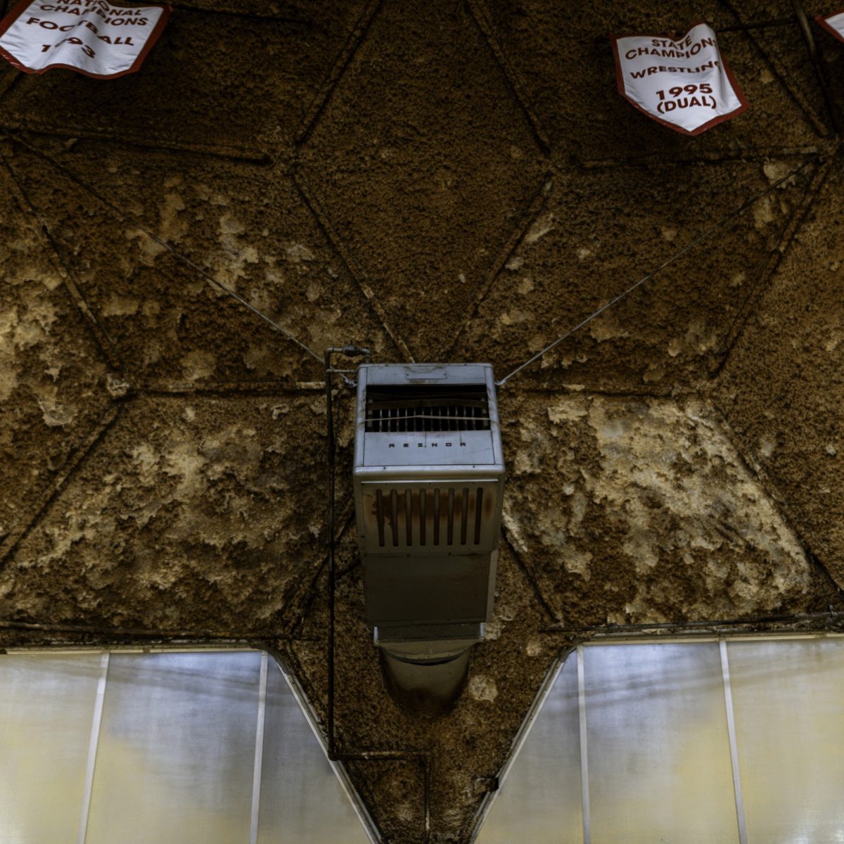 Vertical shot of a gray heater box mounted high on the Dome wall, surrounded by flaking, textured brown ceiling material with championship banners partially visible at the top edge.