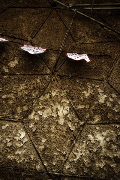 Detail shot looking up at the Dome’s hexagon-patterned ceiling, where rough, mottled brown material and pipes cross above two red and white banners that bend away from the surface.