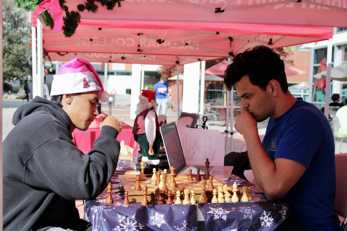 Two male college students sitting on either side of a chess board.