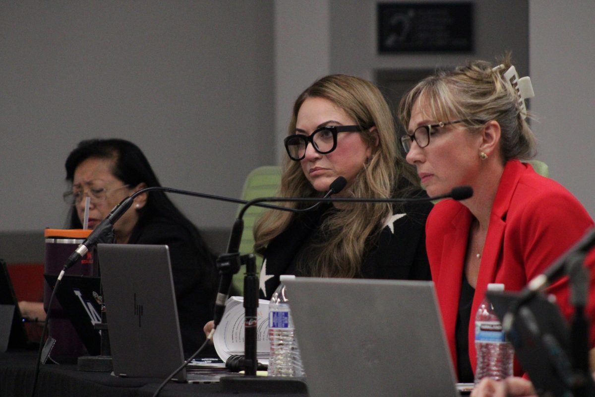 Three Palomar College trustees sit at a dais with microphones and laptops, listening during a board meeting.
