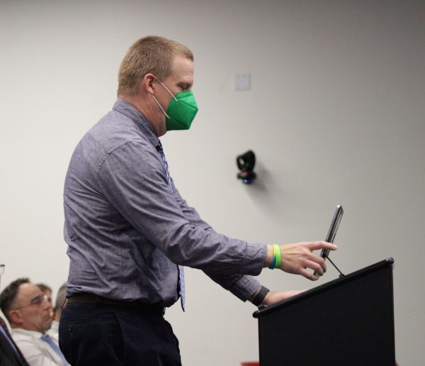 A man wearing a green face mask stands at a podium and speaks to the Palomar College Governing Board.