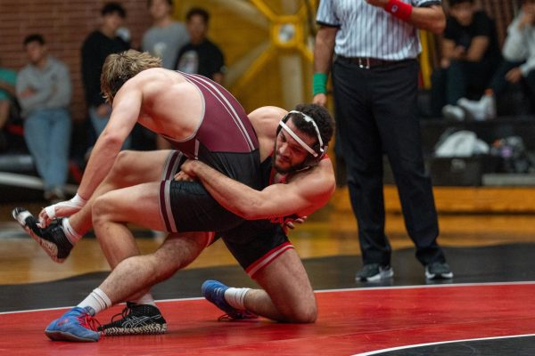 Palomar wrestler Jakar Carter in a black singlet is on his left knee as he grapples another wrestler in a crimson singlet, throwing him over his right leg on October 8, 2025 at the Dome at Palomar College.
