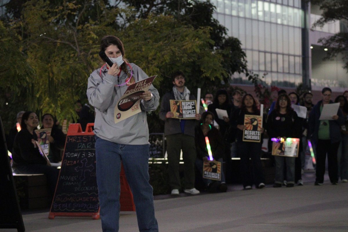 Jena Kruhmin is standing with her hand on her mask, reading a chant to the crowd.