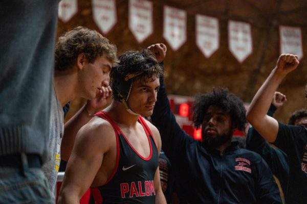 Palomar wrestler, Seth Iten in a black and red singlet stares to the right at his opponent, unseen, as Iten's teammates support him with their right fists raised on Oct. 8, 2025 at Palomar College