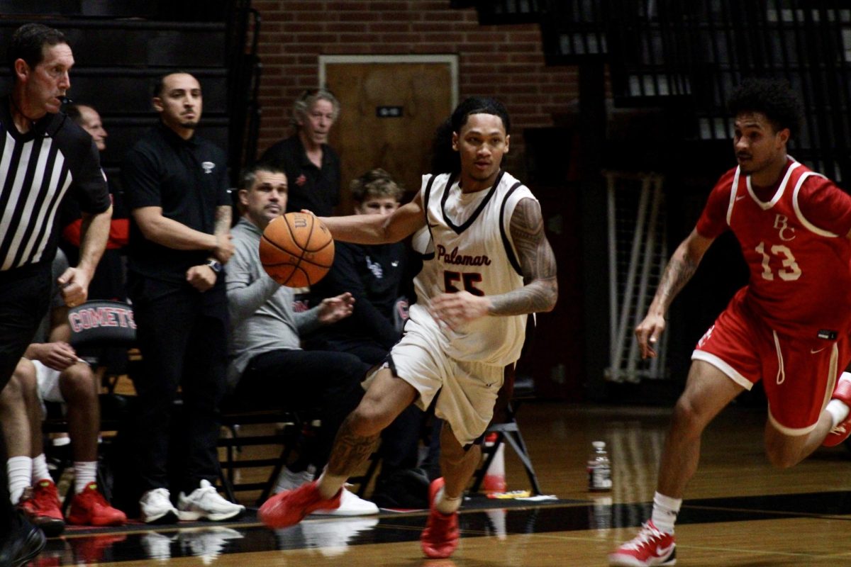 Jaidyn Norman (#55) has the basketball in his right hand and is dribbling it away from his opponent, who is catching up to Norman.