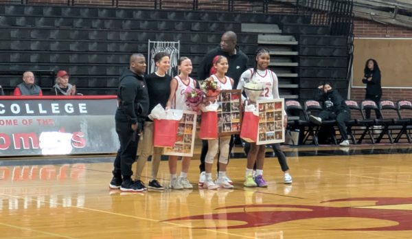 Three Palomar Comet women's basketball players in white uniforms stand side by side with three of their coaches at center court during a ceremony for the three sophomores prior to their game against MiraCosta on Feb. 20 at the Dome.