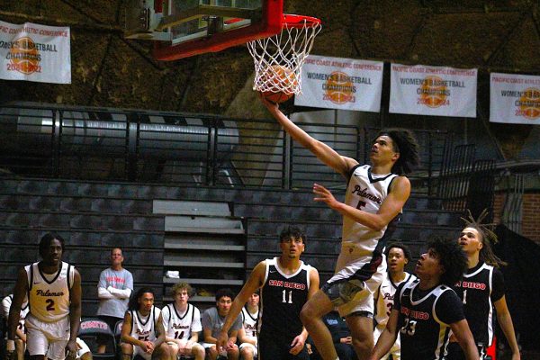 Palomar Comet basketball player Isaiah Pomare in a white uniform drives in for a layup, and shoots with his right hand while San Diego City players in black uniforms stare up at the rim.