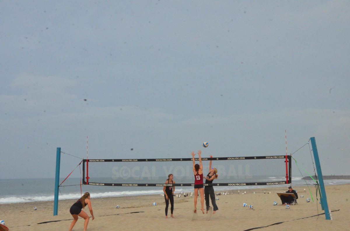Women's beach volleyball player Reese Maffitt in red jumps to block a hit by Caden Pinto in black during a practice match on Feb. 10 at Warmwaters Beach in Carlsbad.