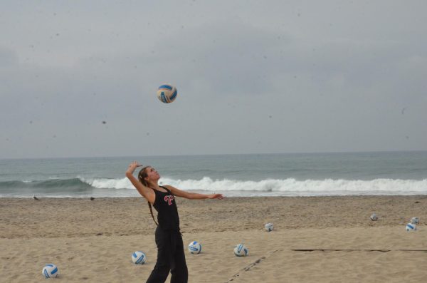 Palomar women’s beach volleyball player Kiana Merrill in a black tank top and pants prepares to serve an airborne volleyball during a Feb. 10 practice at Warmwaters Beach in Carlsbad.