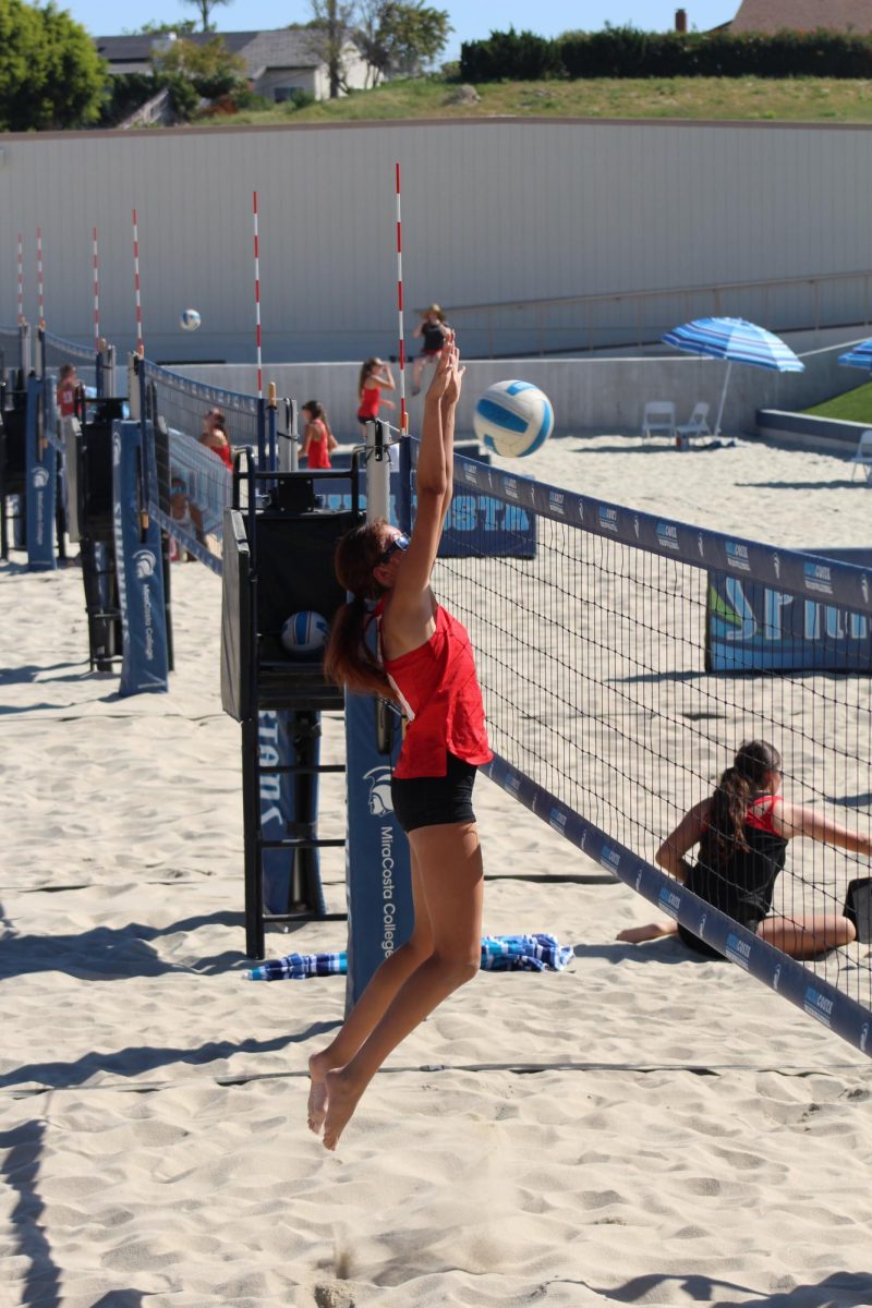 Palomar Comets beach volleyball player in red reaches up as she jumps to block a back-court hit by Mt San Jacinto during a game