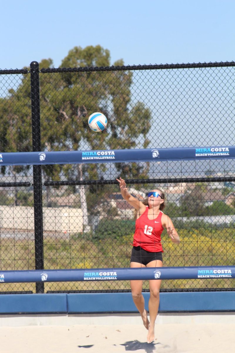 Palomar beach volleyball captain Emma Bambe (#12) in red hits a serve at her opponents.