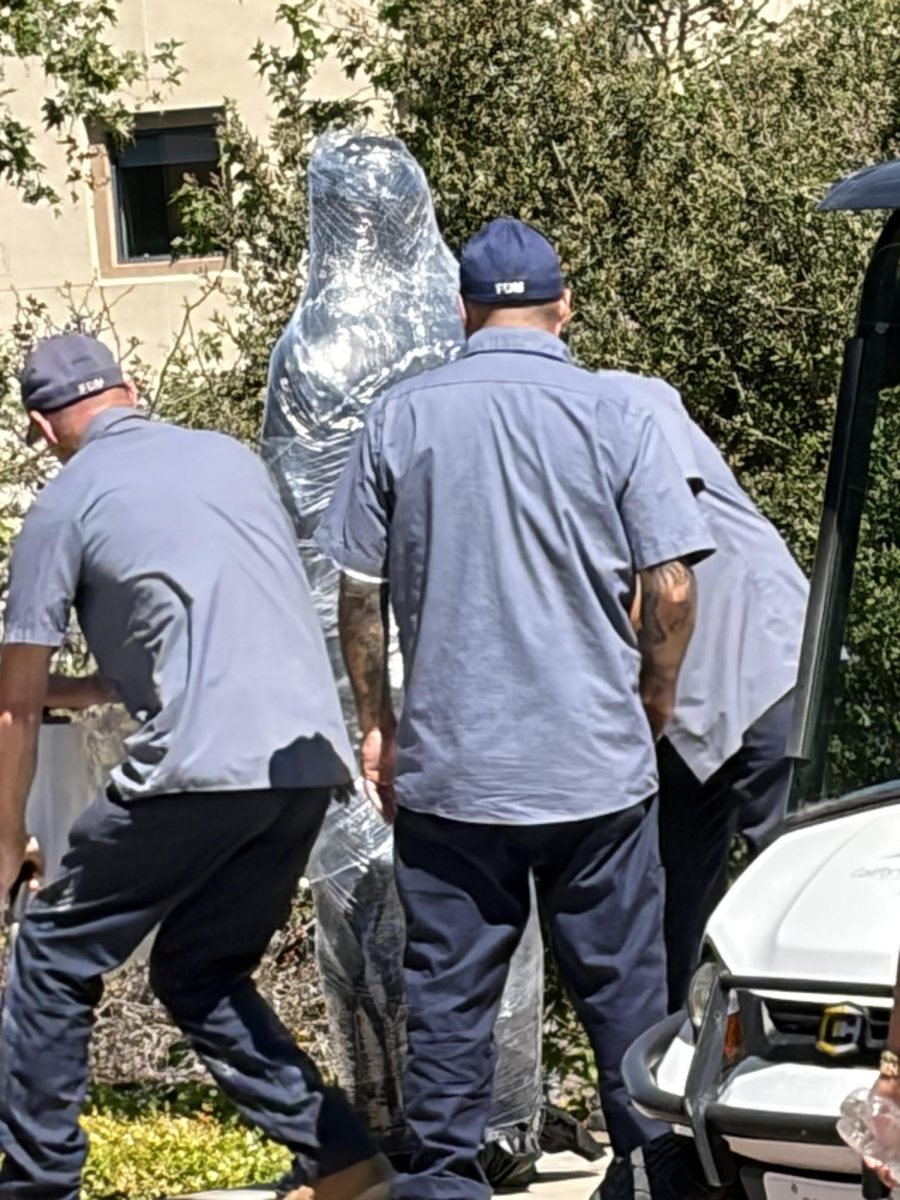three workers in blue cover a bronze statue in clear plastic
