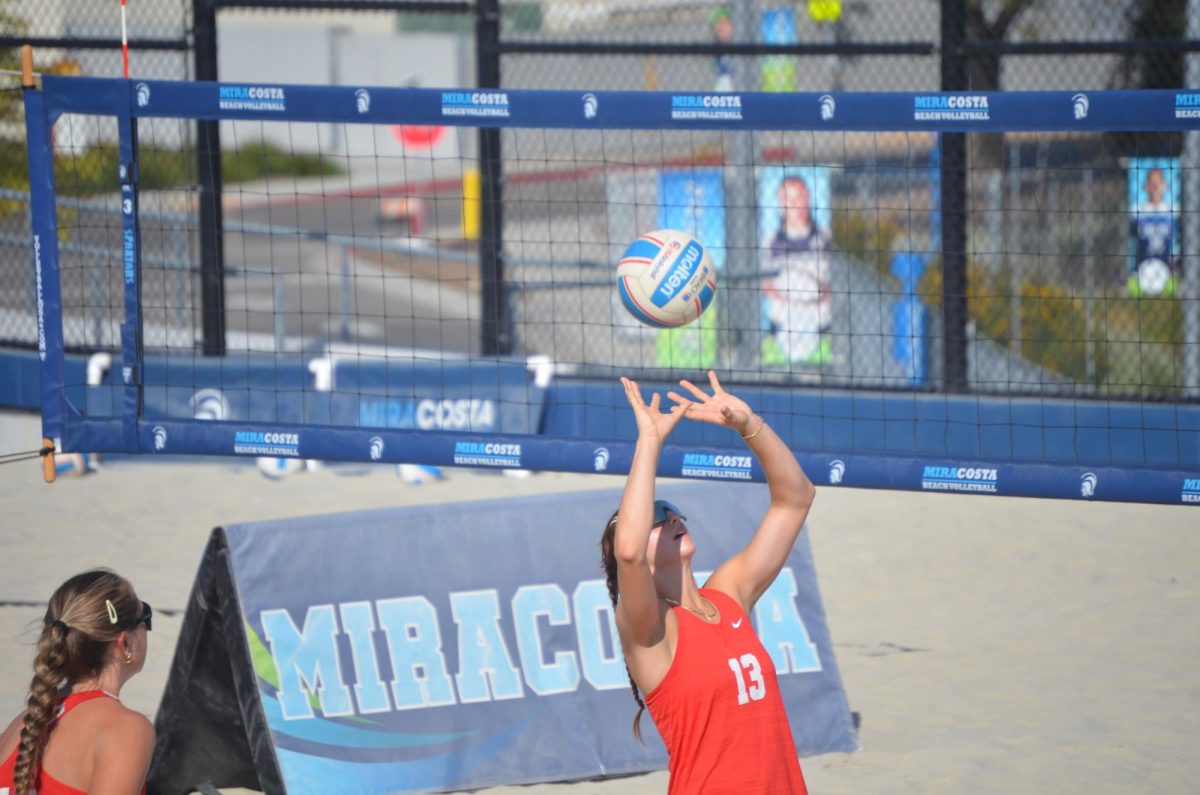 Beach volleyball player Reese Maffitt in a red tank top number 13 prepares to set the airborne volleyball to her teammate for a spike.