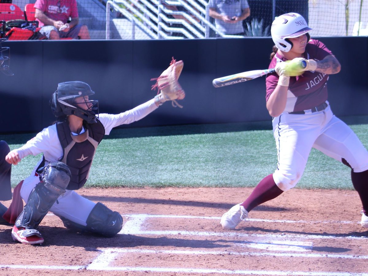 Jaguar softball player in a maroon uniform prepares to swing at a ball.