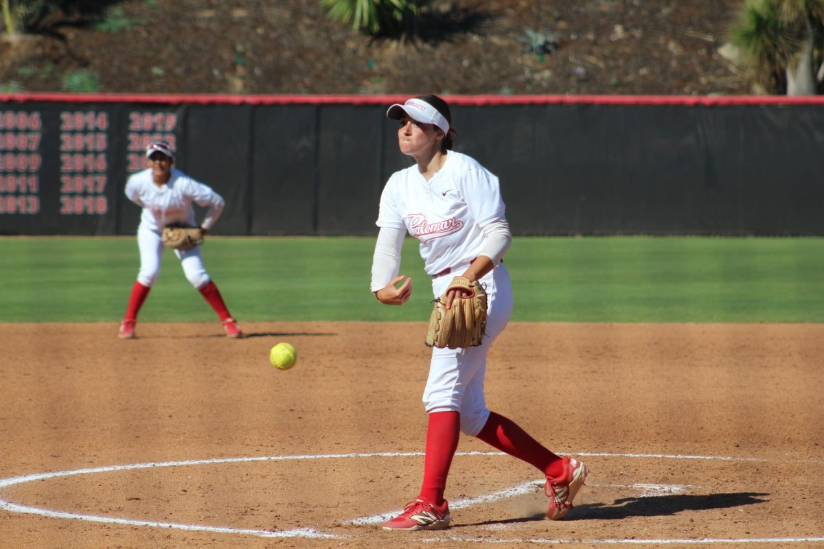 Palomar softball player in a white uniform pitches a yellow softball.