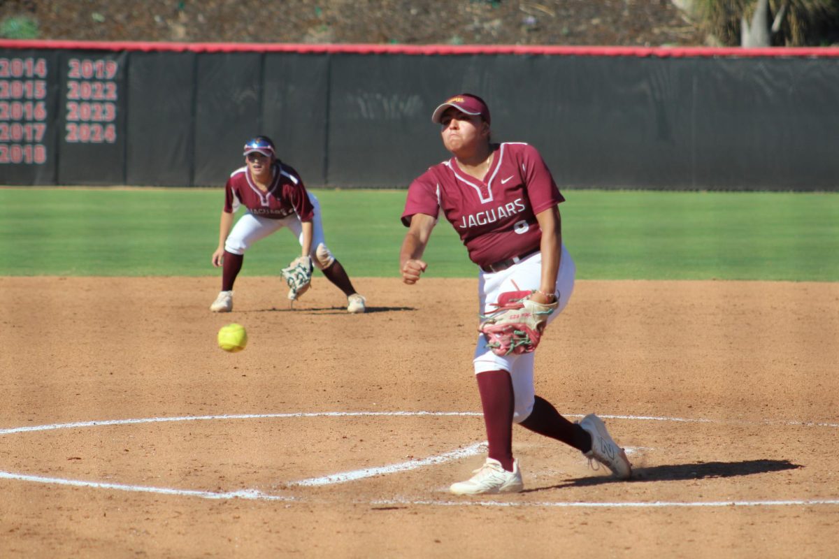 Softball pitcher in a maroon uniform number 6 pitches a bright yellow softball.