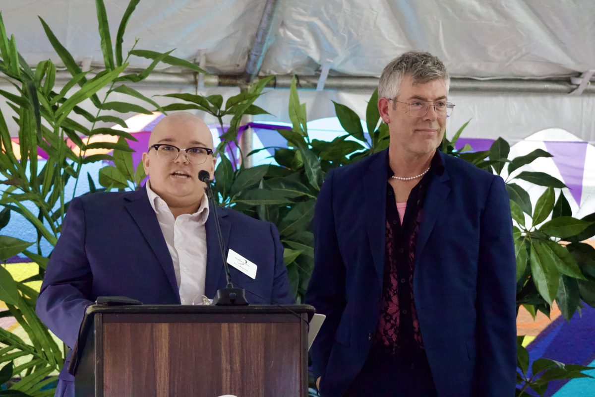 Lene Reynolds and Ben Mudgett are standing behind the podium looking at the audience.