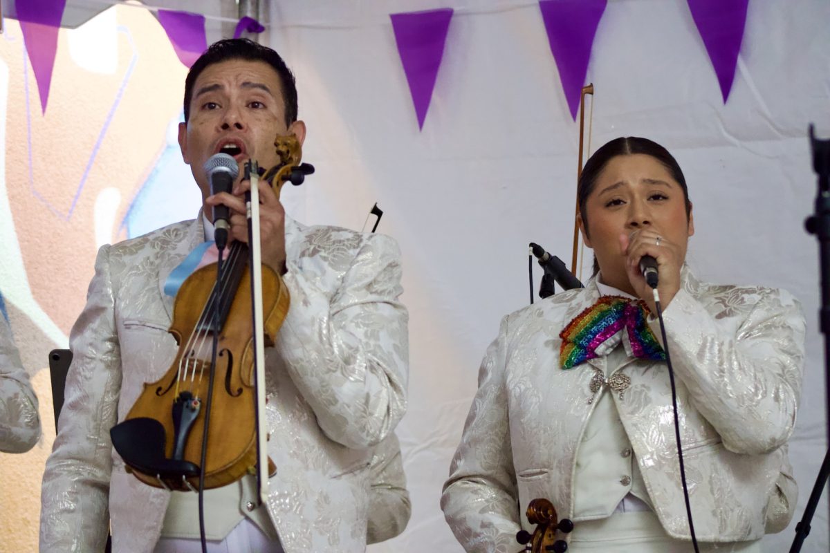 Carlos Samaniego and Melissa Díaz are in white suits, singing and holding their violins.