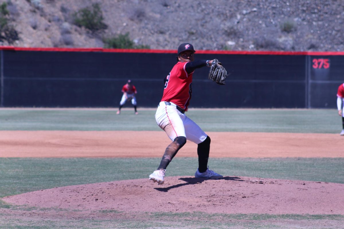 Comet baseball pitcher in a red jersey and black cap prepares to throw a pitch.