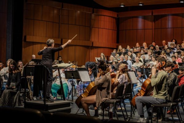 Ellen Weller, a female conductor leads the orchestra and choir during a rehearsal.