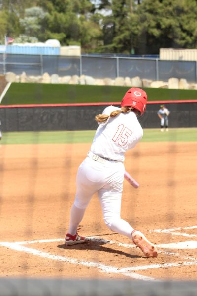 Palomar softball player Alexis Huey in a white jersey number 15 swings her bat at a pitch which resulted in a home run.