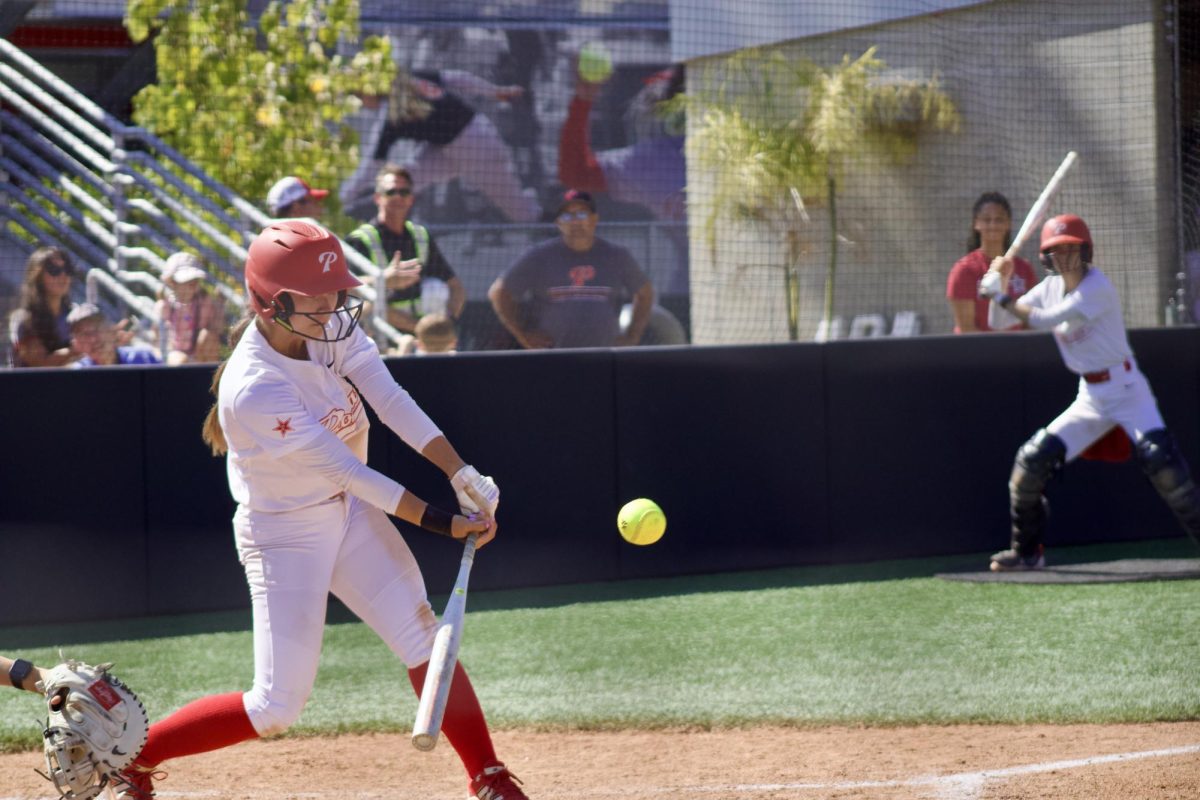 Palomar softball player in a white uniform swings and sends the ball to right field.