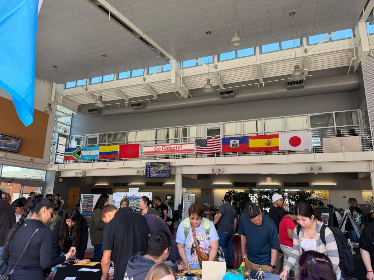 An indoor college event with people interacting with tables and international flags displayed above.