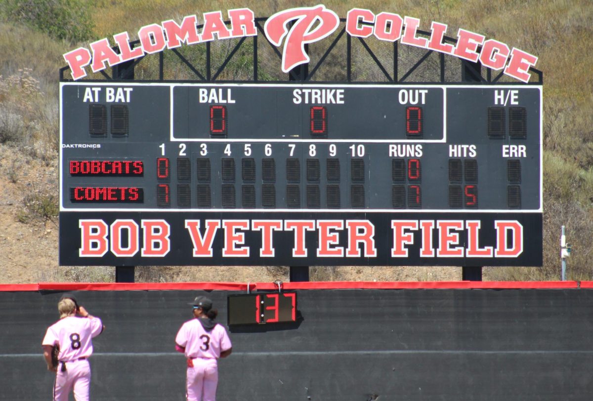 A scoreboard reading Comets: 7 Bobcats: 0 with Bob Vetter Field at the bottom looms as two Comet baseball players in pink uniforms numbers 8 and 3 head to left and center field.